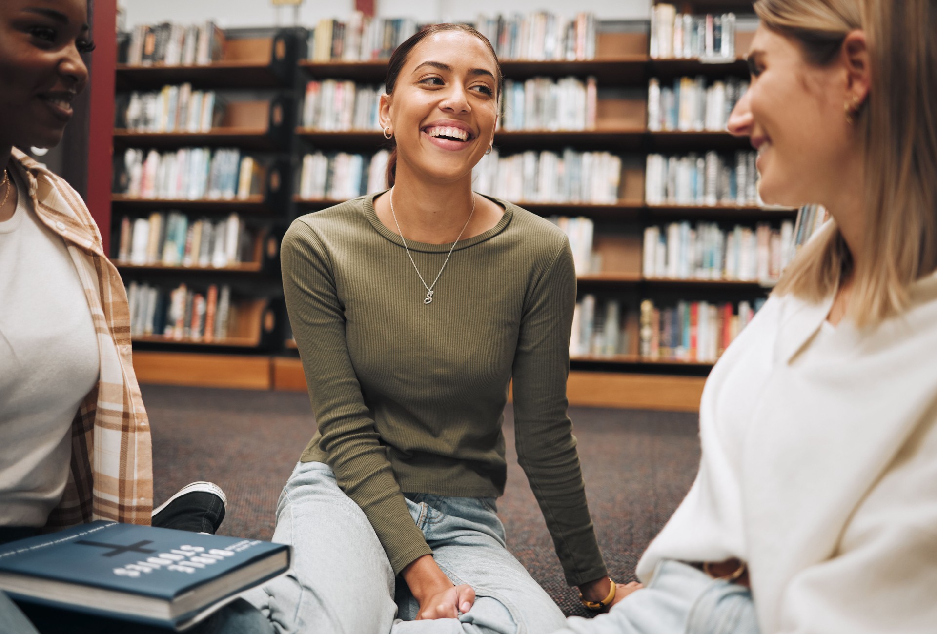 Student, friends and book discussion in library with smile for education, learning or knowledge at university. Group of happy women enjoy conversation, book club or social study for research project